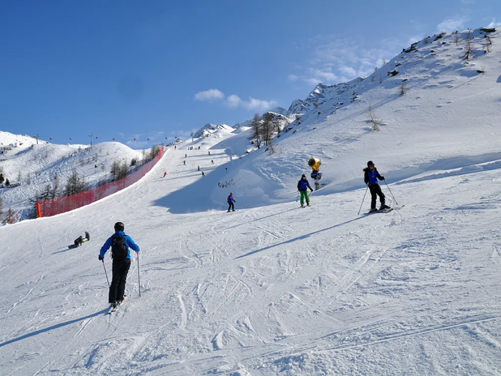 Skifahrende auf einer breiten Piste unter blauem Himmel.